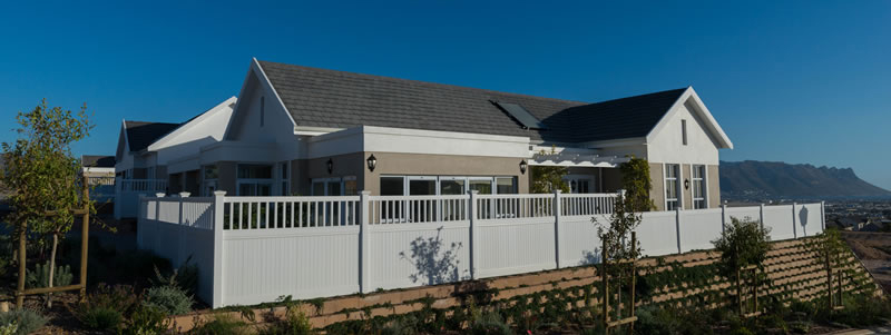House on a level hillside platform held up by a planted block retaining wall, mountains behind