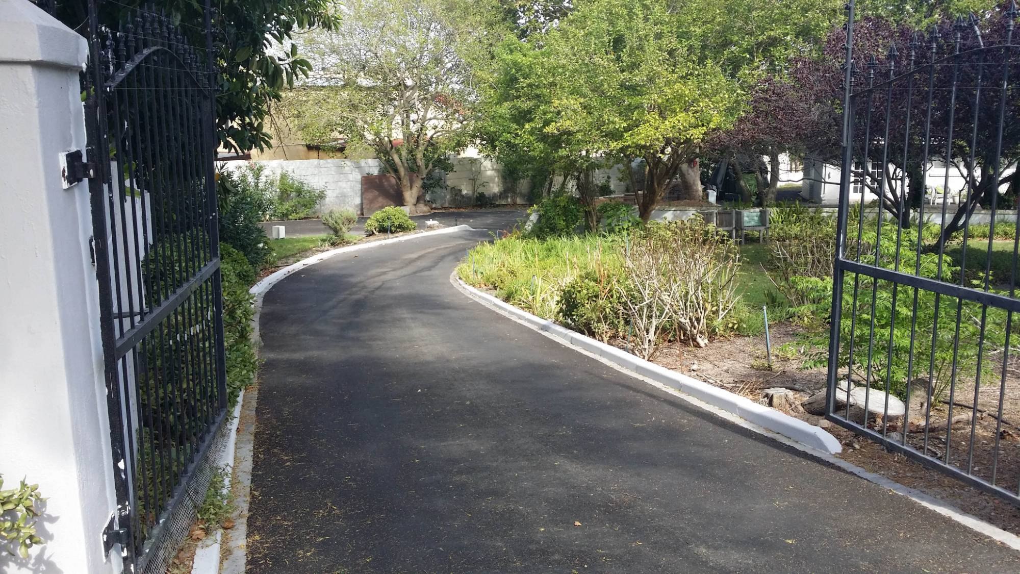 Freshly tarred driveway curving through open gates, edged with white kerbs