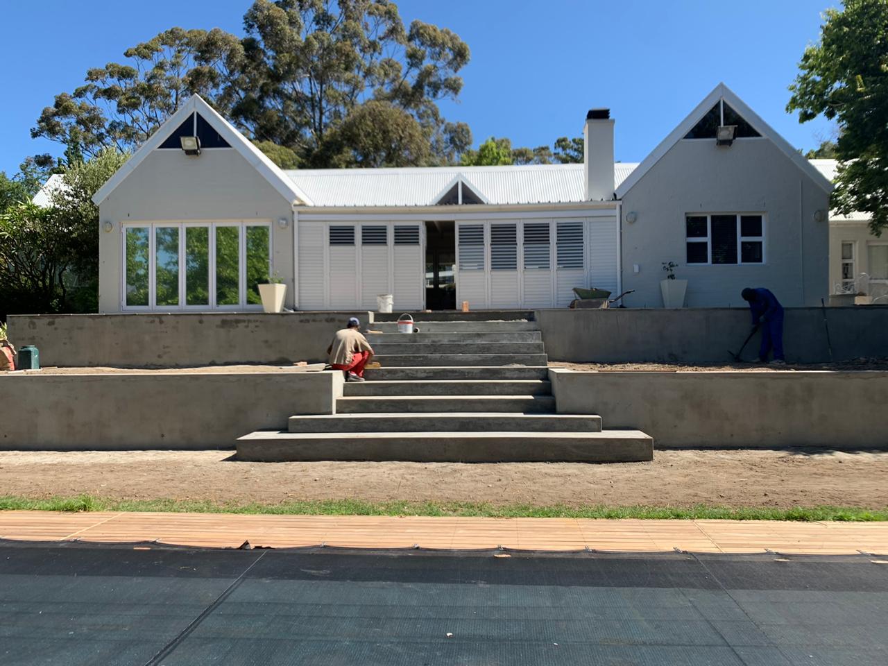 Crew finishing two tiers of concrete retaining walls and wide steps in front of a house