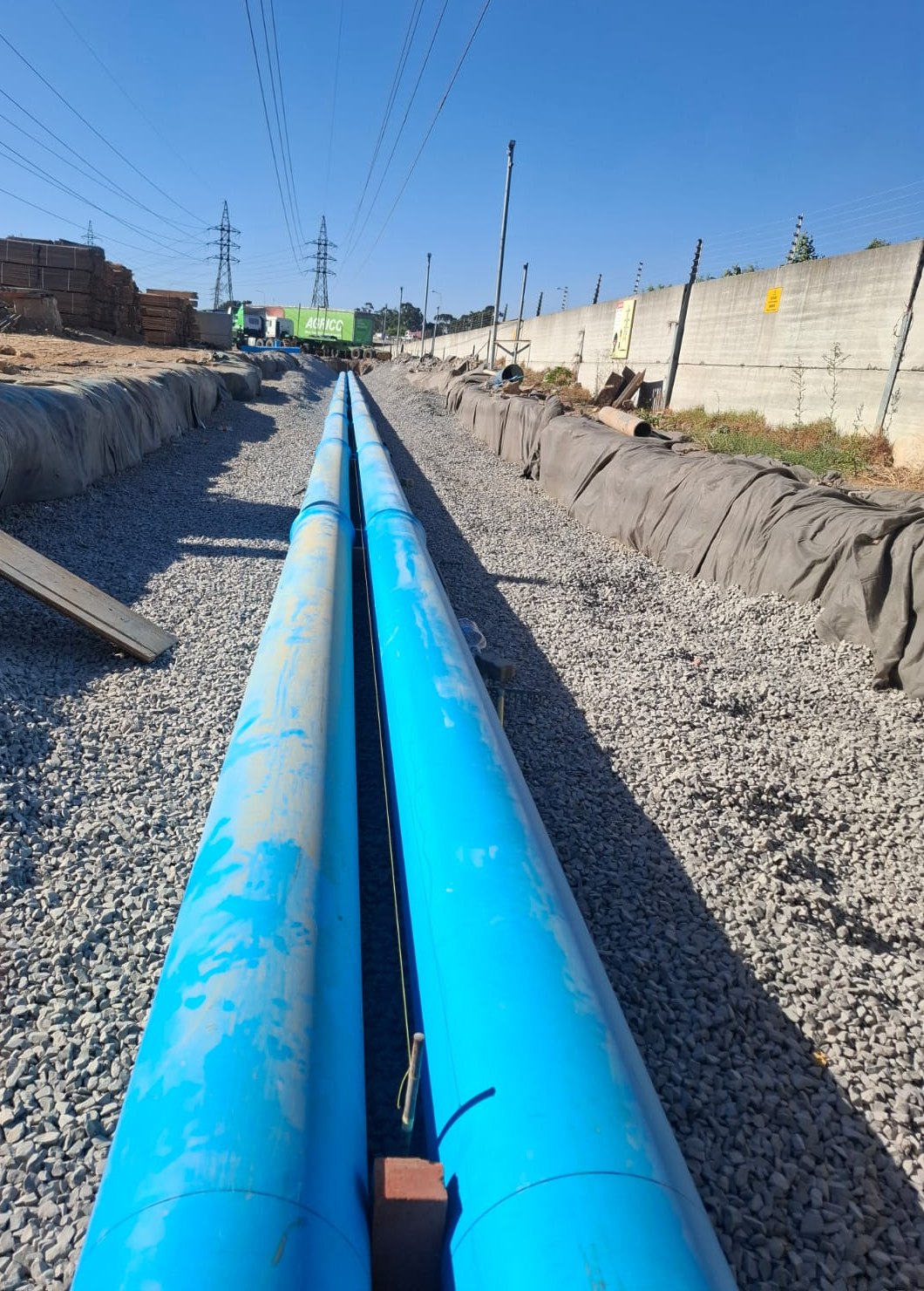 Twin blue pipelines laid on crushed stone in a long trench lined with geofabric